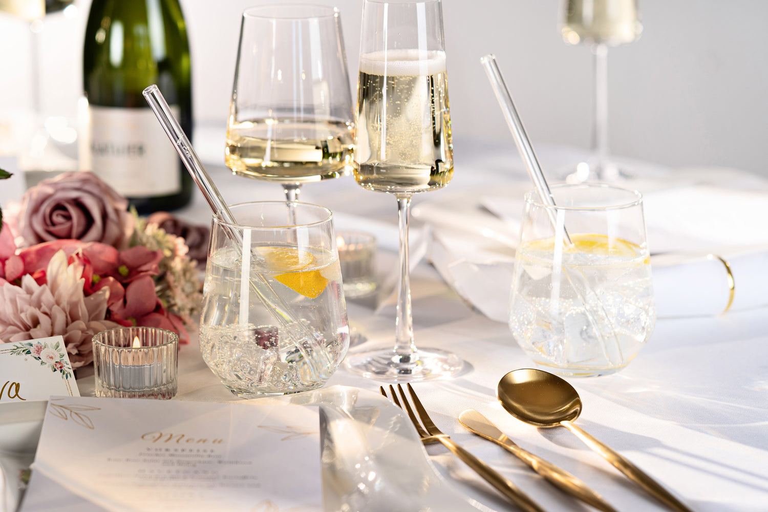 Hochzeitstisch mit Getränken, Blumenschmuck und personalisierten Glastrinkhalmen mit Gravur im sanften Licht.
