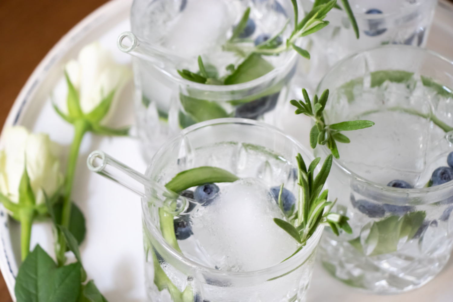 Erfrischende Getränke mit Glasstrohhalmen, Hochzeitsdeko und Blumen im Hintergrund.