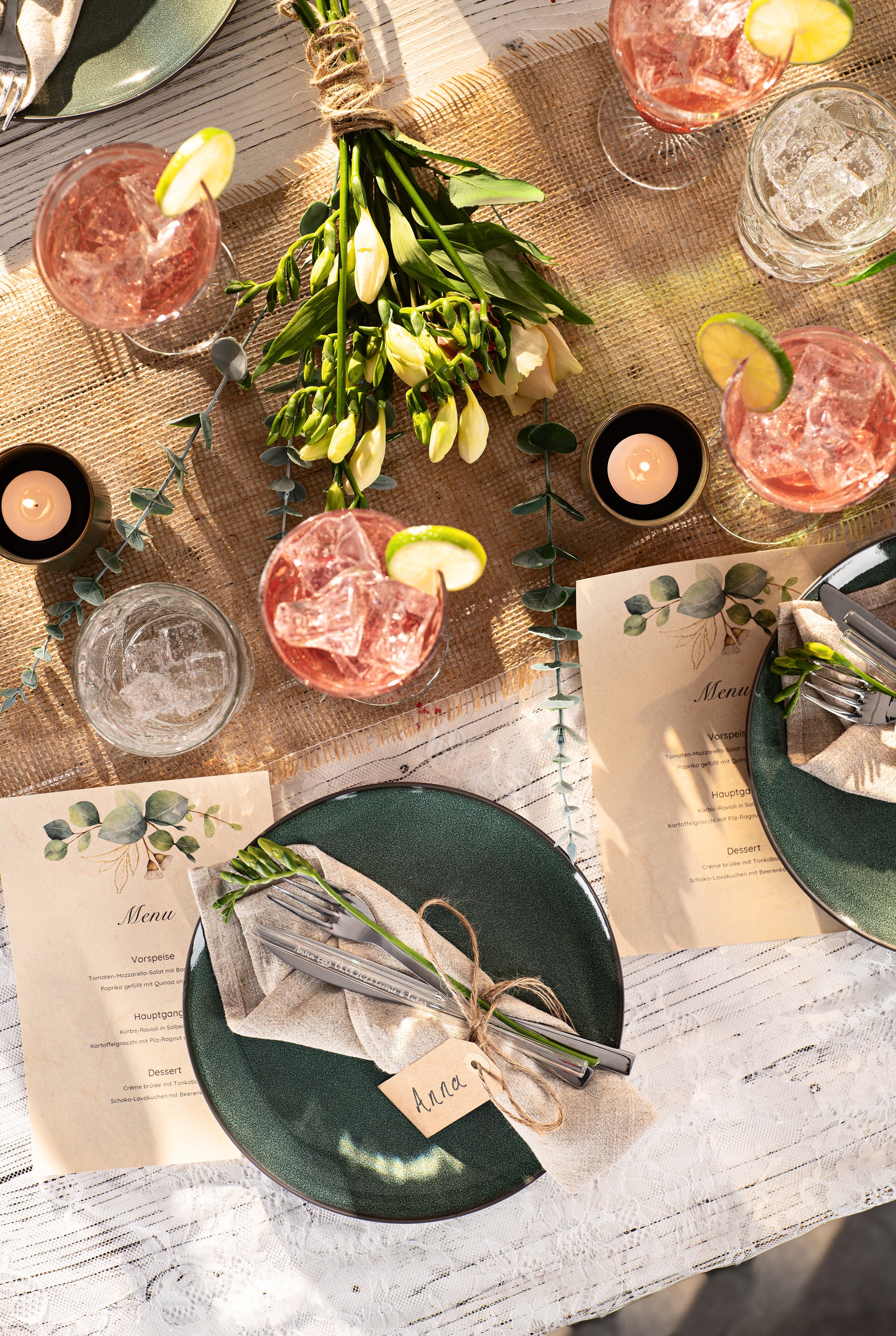 Hochzeits-Tischdekoration mit Getränken, Blumenstrauß, Gastgeschenk und Menükarten im Sonnenlicht.
